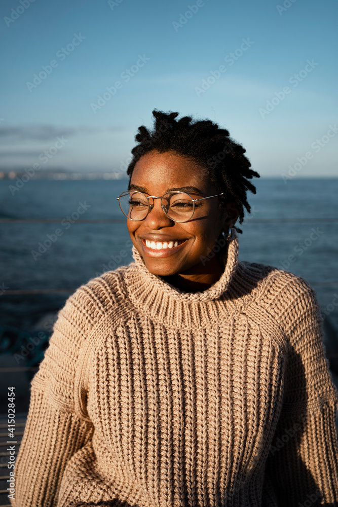 Smiling woman wearing eyeglasses looking away while sitting against sea Smiling woman wearing eyeglasses looking away while sitting against sea