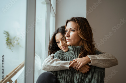 Daughter embracing mother while contemplating by window at home photo