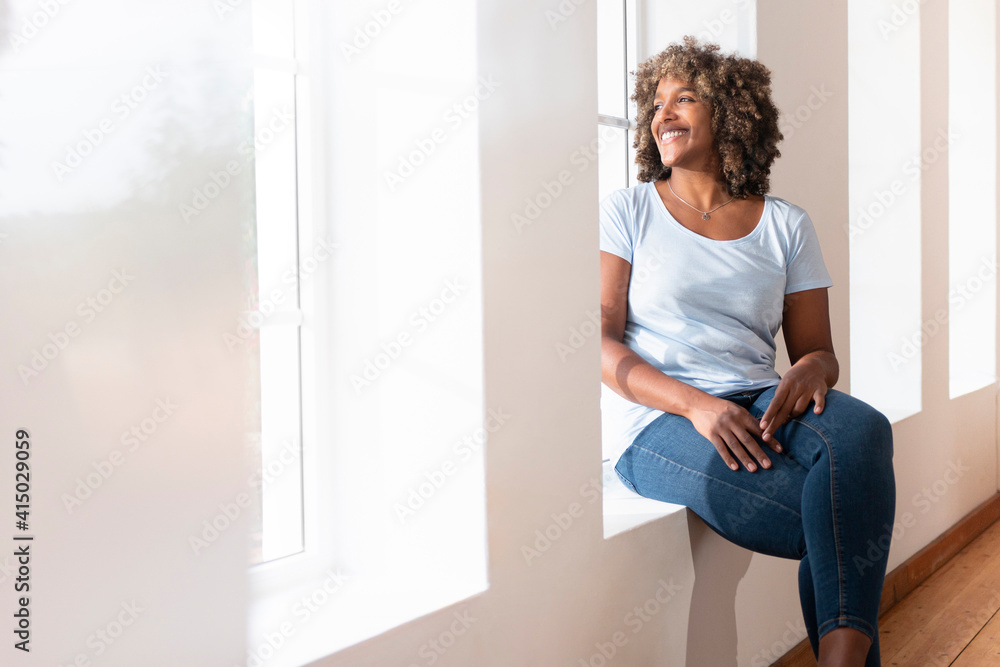 Mid adult woman looking away while sitting on window sill at home