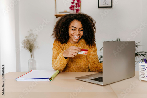 Young woman with credit card using laptop while sitting at home office photo