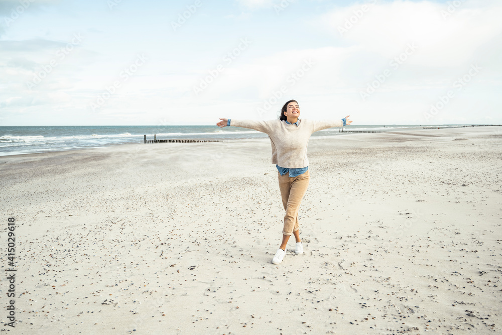 Portrait of young woman walking on sandy beach with raised arms Portrait of young woman walking on sandy beach with raised arms