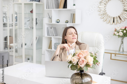 a young female coach works in a home office in a light interior with a laptop and flowers on the table, the concept of remote work