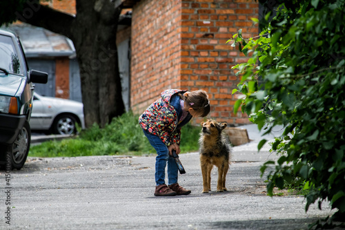 Baby girl leaned towards a stray dog ​​and explains something to her. The dog listens attentively to the girl