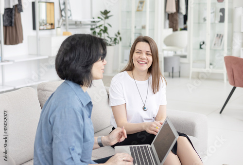 two young women conduct a coaching session in home office in light interior with laptop and flowers on tablework with metaphorical cards and psychological counseling