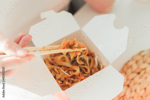 Wok noodles in takeaway box. Woman eating shrimps with chopsticks, close up view on female hands.