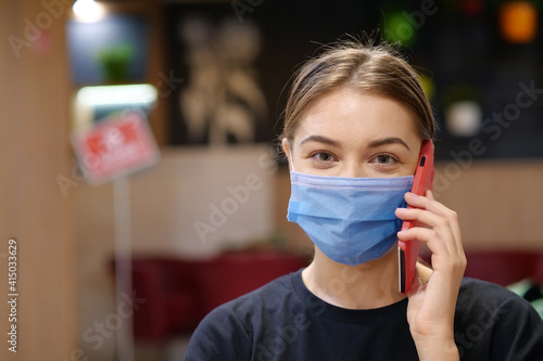 Young girl in blue medical protective mask talks on smartphone inside restaurant photo