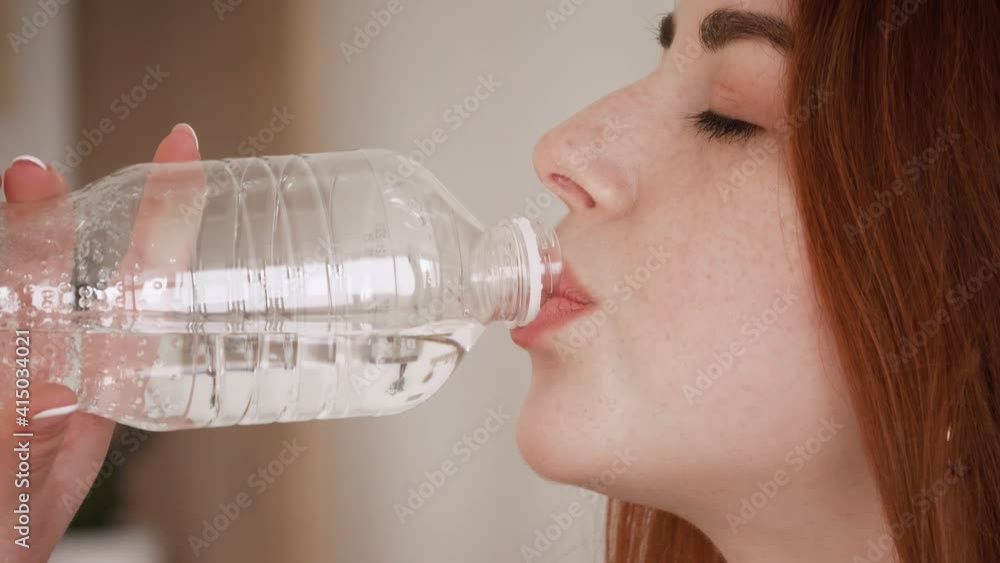 fitness red hair girl drinking from sport bottle during a workout pause at home or gym. Close portrait of active woman drinking from water bottle while resting from training fitness red hair girl drinking from sport bottle during a workout pause at home or gym. Close portrait of active woman drinking from water bottle while resting from training