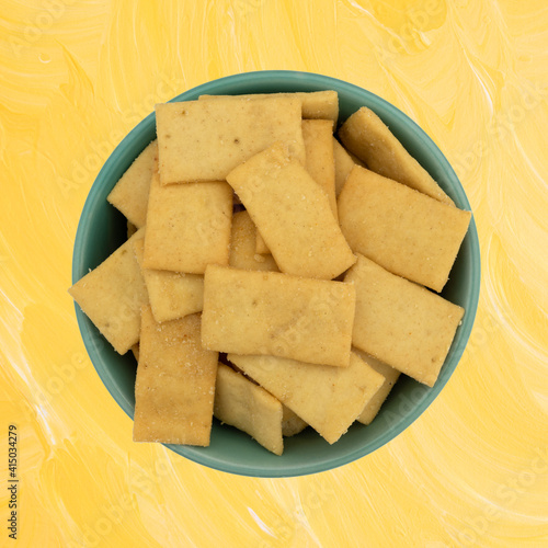 Cheese and garlic snack crackers in a green bowl on a yellow painted wood background top view.