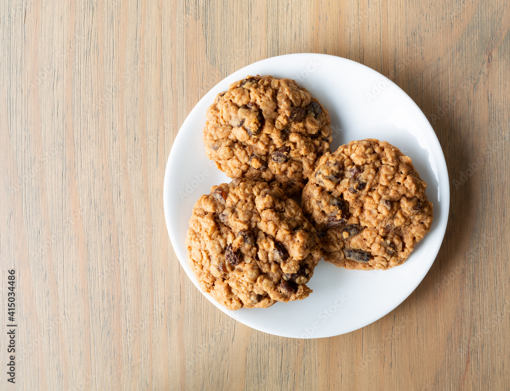 Top view of homemade oatmeal raisin cookies on a white plate atop a table illuminated with natural light.