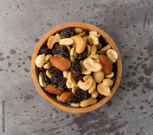 Assortment of nuts and dried fruit in a wood bowl atop a gray background top view.