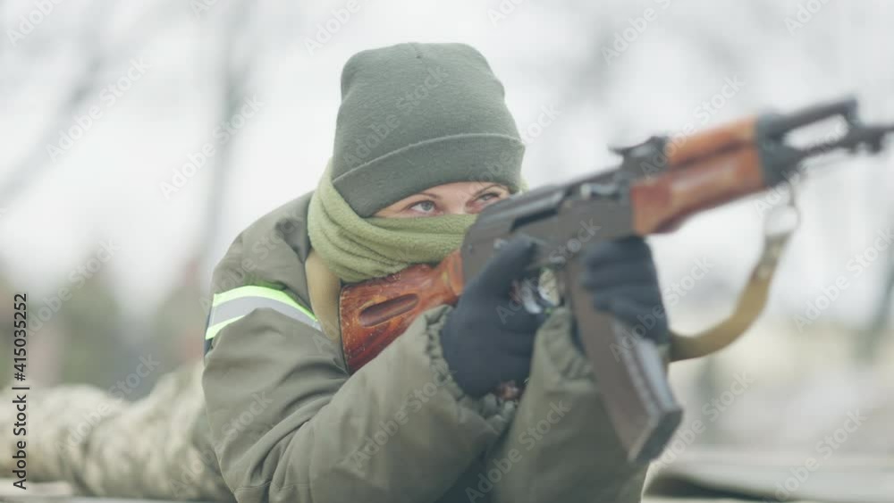 Masked female Caucasian soldier reloading gun and aiming lying on ...