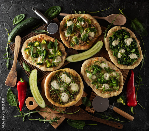 Green pizzas overhead view with cucumbers, paprika, spinach, wooden spatula and pizza cutter