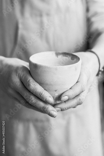 person in the apron holding handmade clay and turquoise cup of tea