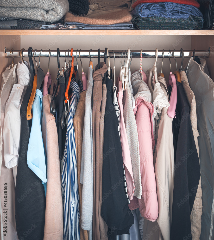 Women's clothing hangs on hangers in the closet. Wardrobe with different clothes, household items, a selection of clothes in the closet.