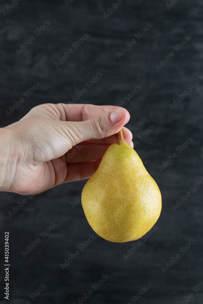 A person holding a yellow pear from the stem A person holding a yellow pear from the stem