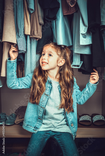 Funny little girl having fun in the wardrobe with clothes. Processing with tinting, vertical view. © Helga1