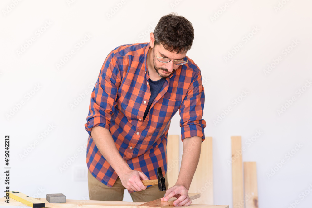 Man driving a nail into a table on a workbench Man driving a nail into a table on a workbench