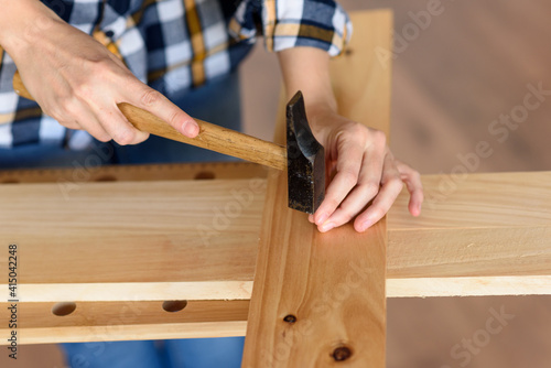 Close up of young woman assembling furniture at home working with hammer. DIY concept