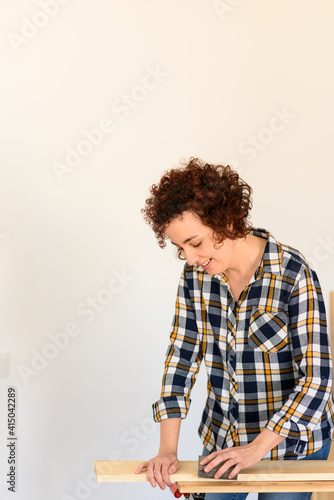 Woman sanding wood on a workbench with white background inside a floor.