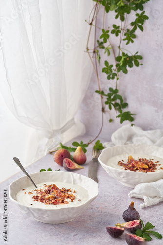 Ceramic bowls with delicious porridge and sweet fig slices on top for breakfast against creeping plant photo