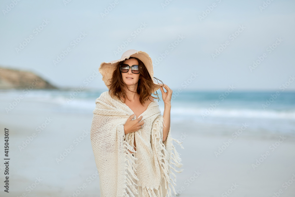 Female traveler in sunglasses and hat walking along seashore and looking at camera Female traveler in sunglasses and hat walking along seashore and looking at camera