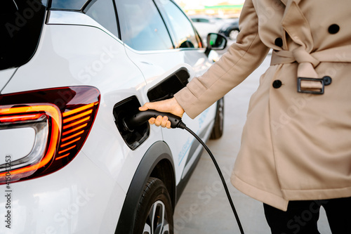 Crop of stylish male entrepreneur browsing smartphone while standing at petrol station and refueling automobile photo