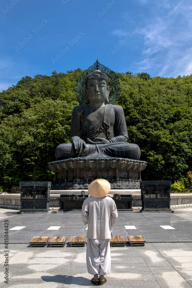 Back view of unrecognizable person in cone hat standing in front of Sinheungsa temple with huge statue of Buddha in Seoraksan National Park Back view of unrecognizable person in cone hat standing in front of Sinheungsa temple with huge statue of Buddha in Seoraksan National Park