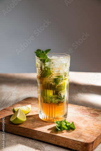 Refreshing cold alcoholic mojito with ice mint leaves and cut lime on wooden board photo