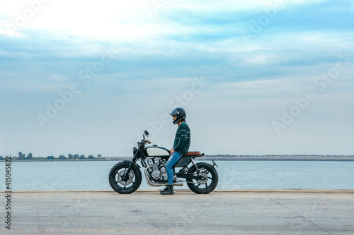 Side view of unrecognizable male biker in casual outfit and protective helmet sitting on motorcycle on embankment near sea at construction site photo