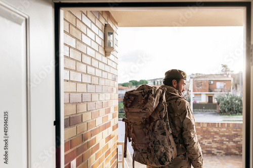 Back view of male soldier with backpack and in military uniform standing at doorway before departure photo