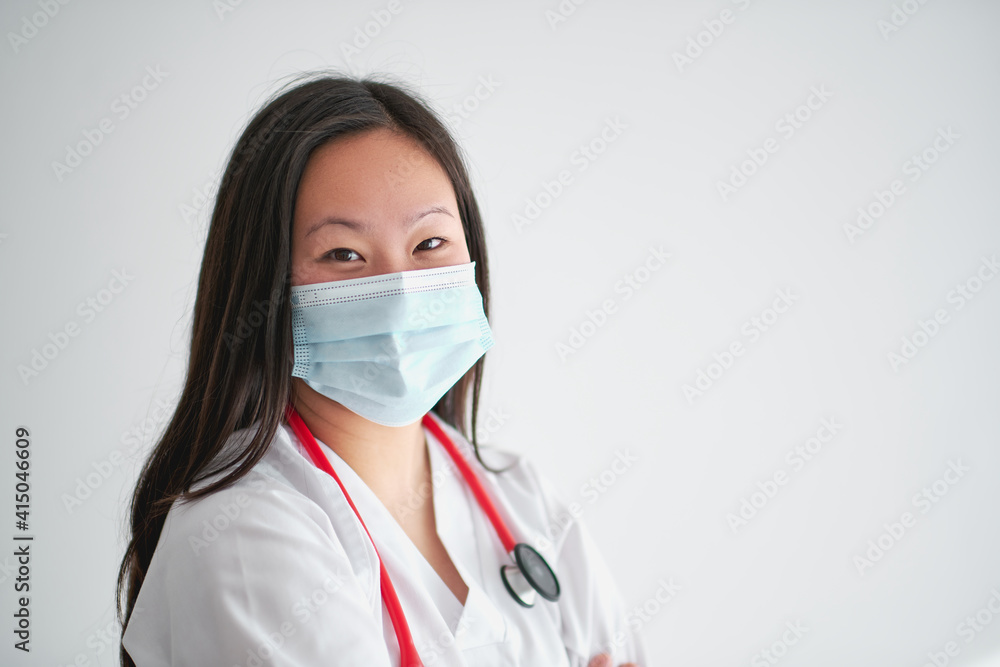 Stock photo of young female doctor wearing face mask and working from home due to covid19 smiling and looking at camera. Stock photo of young female doctor wearing face mask and working from home due to covid19 smiling and looking at camera.