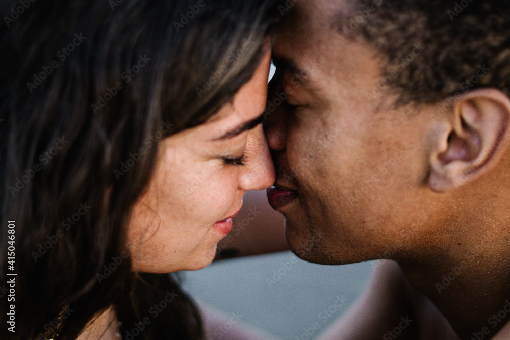 African American male traveler kissing sincere female partner standing against ocean during summer trip African American male traveler kissing sincere female partner standing against ocean during summer trip