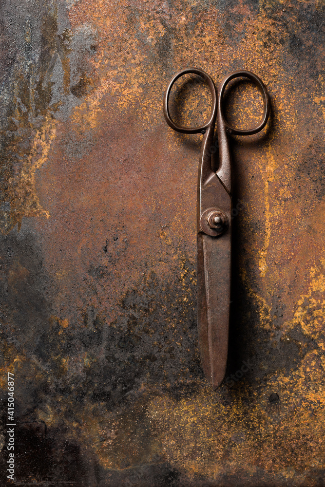 Top view of old metal scissors placed on dark table with rusty surface