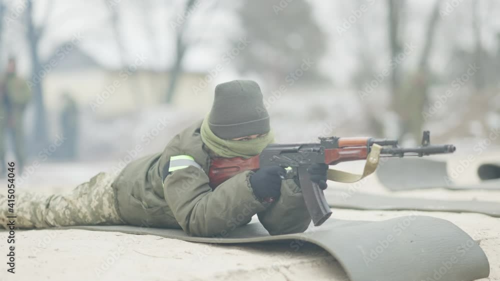 Serious confident female soldier lying on polygon shooting in slow motion from rifled army gun. Portrait of professional Caucasian military woman training outdoors. Serious confident female soldier lying on polygon shooting in slow motion from rifled army gun. Portrait of professional Caucasian military woman training outdoors.