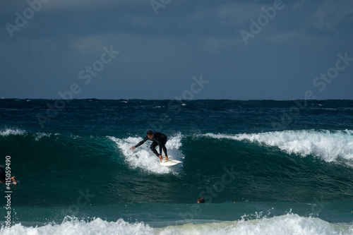 Male surfer catching a wave and doing a turn wearing a black wetsuit in winter time