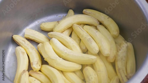 A pot of matoke a type of African banana used for cooking and an African woman's hand throwing a freshly peeled on in the pot.