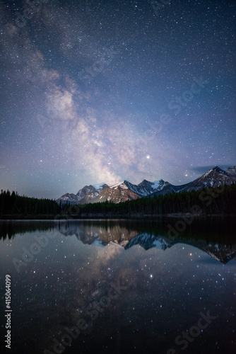 The Milky Way reflecting off of the calm waters of Herbert Lake while the town of Lake Louise illuminated the Canadian Rockies. photo