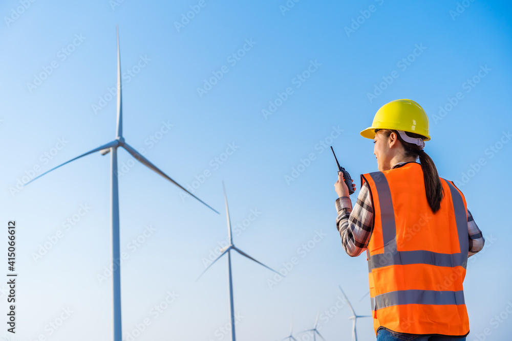 female engineer using walkie talkie to checking system against wind turbine farm female engineer using walkie talkie to checking system against wind turbine farm