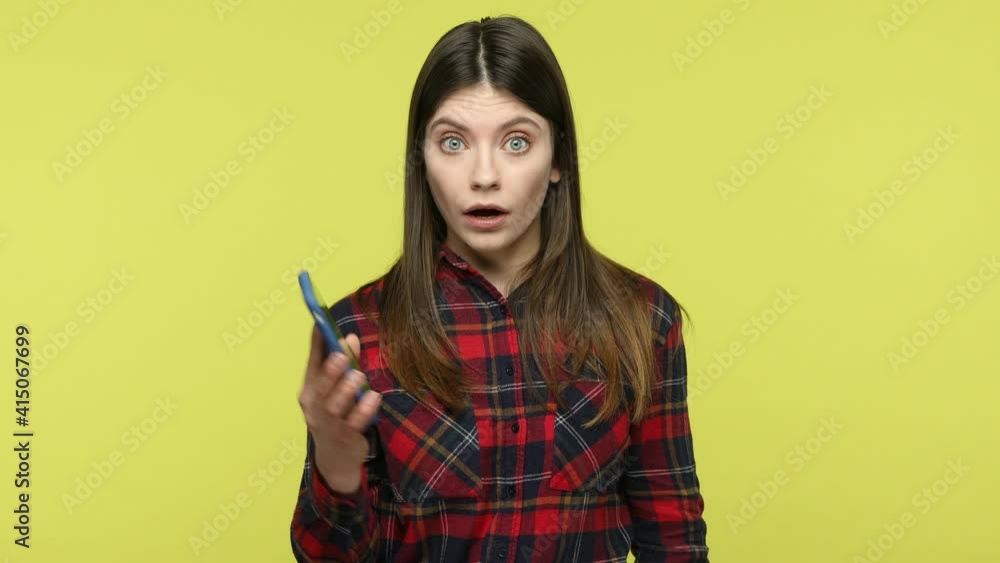 Surprised amazed woman in checkered shirt holding and showing smartphone with green screen display, shocked with web site content, programm features. Indoor studio shot isolated on yellow background Surprised amazed woman in checkered shirt holding and showing smartphone with green screen display, shocked with web site content, programm features. Indoor studio shot isolated on yellow background