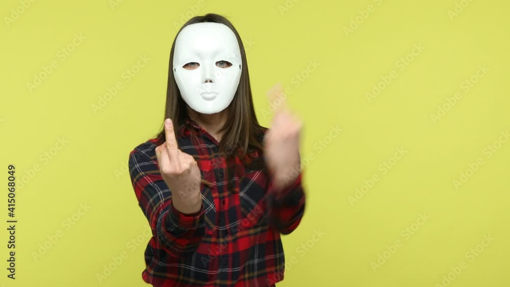 Rude aggressive unknown woman in checkered shirt threatening you hiding her face behind white mask, showing middle finger fuck you gesture, bullying. Indoor studio shot isolated on yellow background Rude aggressive unknown woman in checkered shirt threatening you hiding her face behind white mask, showing middle finger fuck you gesture, bullying. Indoor studio shot isolated on yellow background