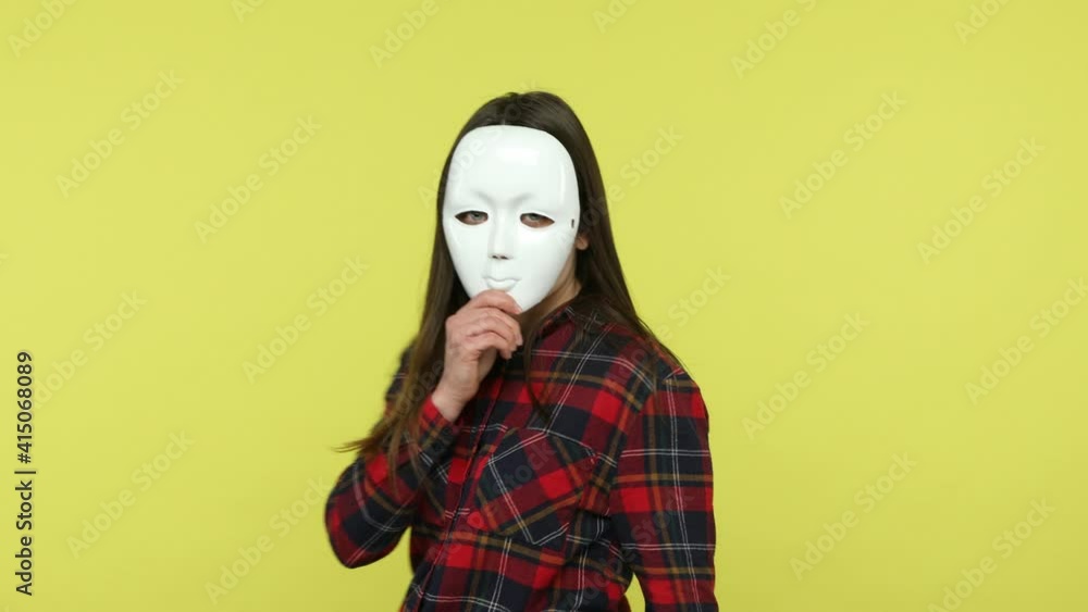 Back view brunette woman in checkered shirt appearing and turning around showing her face covered with white mask hiding her personality, blind dating. Indoor studio shot isolated on yellow background Back view brunette woman in checkered shirt appearing and turning around showing her face covered with white mask hiding her personality, blind dating. Indoor studio shot isolated on yellow background