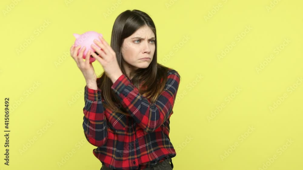 Upset brunette woman shaking empty piggy bank, has no savings, wrong budget planning, frustrated because of low interest on deposit, bankruptcy. Indoor studio shot isolated on yellow background Upset brunette woman shaking empty piggy bank, has no savings, wrong budget planning, frustrated because of low interest on deposit, bankruptcy. Indoor studio shot isolated on yellow background