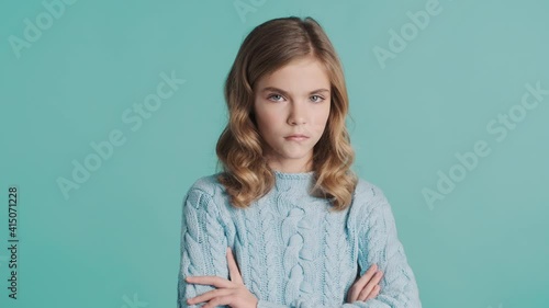 Serious blond teenager girl keeping arms folded offended by hearing bad news looking angry on camera over colorful background