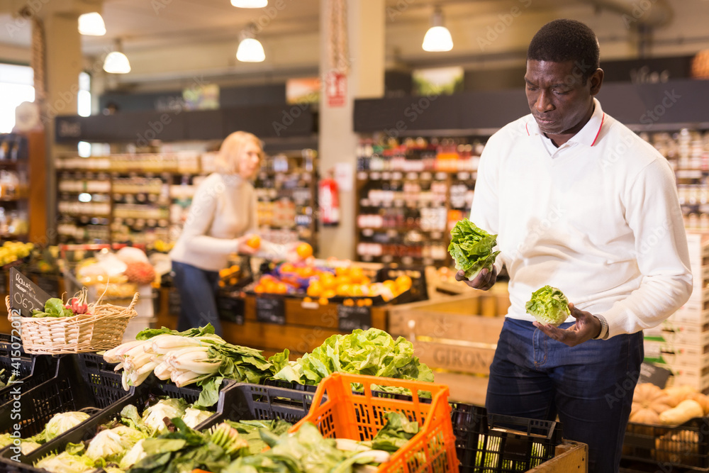 Interested African American man making purchases in grocery store, looking for fresh vegetables