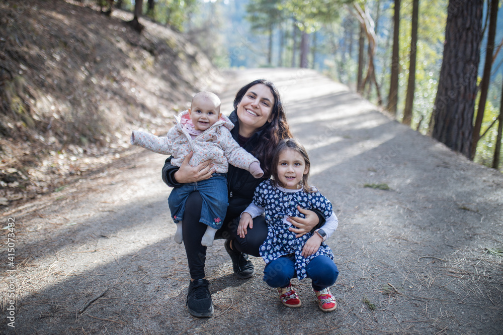 Happy woman holding her adorable young daughters in the forest Happy woman holding her adorable young daughters in the forest