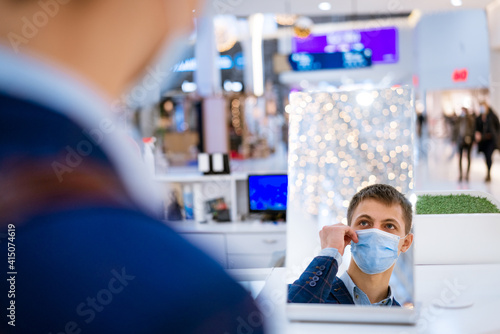 young man putting on a mask while looking in the mirror in the mall