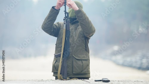 Portrait of focused masked male recruit start disassembling weapon on outdoor polygon. Confident concentrated Caucasian young man unscrewing flash hider on rifled gun. Military army. photo
