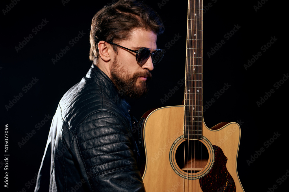 Obraz premium A man with a guitar in his hands leather jacket music performance rock star modern style dark background