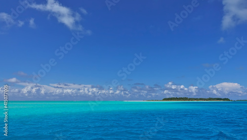 Idyll and paradise in the Maldives. Turquoise and aquamarine ocean hues. Picturesque clouds in the azure sky. In the distance is an island with a sandy beach and tropical vegetation. Endless summer