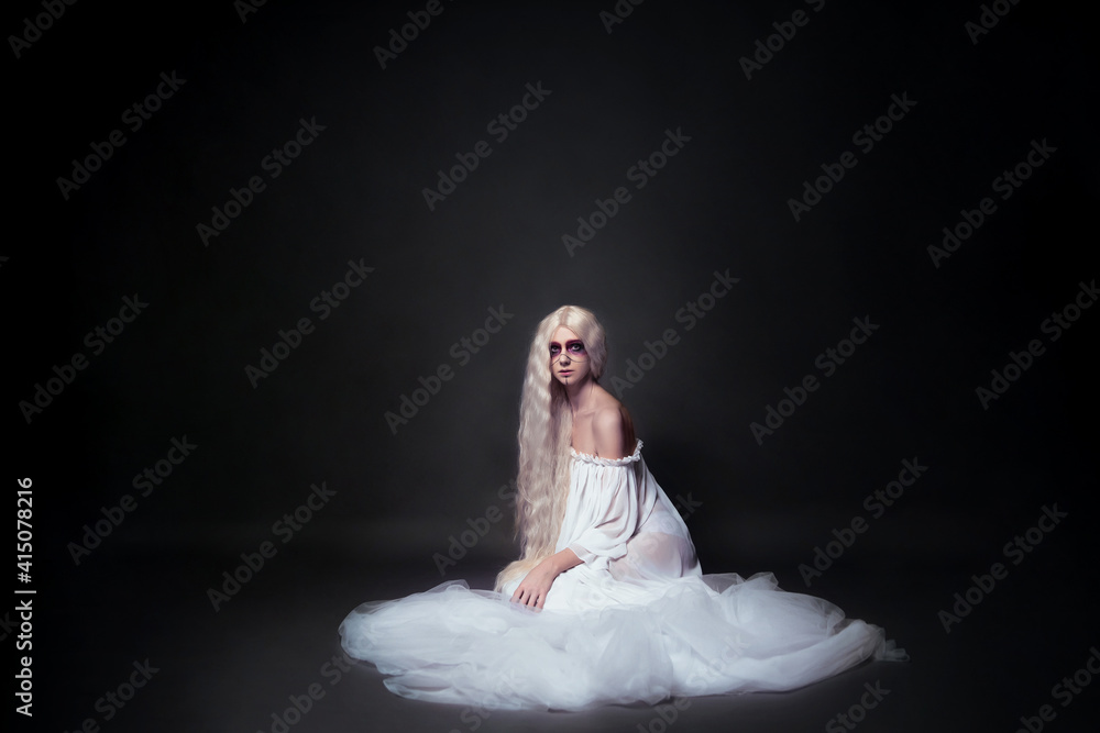 a concept photo of a beautiful young woman with bright makeup who plays the role of a priestess, spirit or ghost for Halloween. She is sitting in a white veil on a black background a concept photo of a beautiful young woman with bright makeup who plays the role of a priestess, spirit or ghost for Halloween. She is sitting in a white veil on a black background